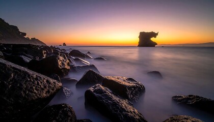 A long-exposure captures a tranquil coastal scene. Soft, blurring water meets dark rocks under a colorful sunset sky, with an island in the distance
