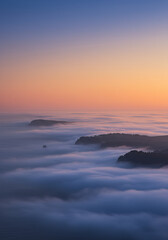 Fototapeta premium Ethereal Sea Fog Rolling Over Forested Headlands at Sunrise