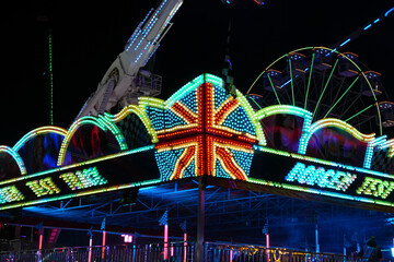 Dazzling funfair rides illuminate the night with a vibrant Union Jack light display and a glowing ferris wheel at Goose Fair, Nottingham, England.