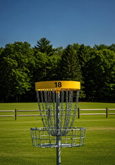 Disc Golf Basket on Field with Lush Green Forest and Blue Skies