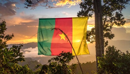 The flag of Cameroon flutters against a scenic sunset background, framed by tree branches. A vibrant display of patriotism and natural beauty