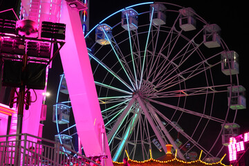 Vibrant Ferris wheel and fairground rides illuminate the night sky at Goose Fair, Nottingham, England, showcasing thrilling entertainment and colorful lights.