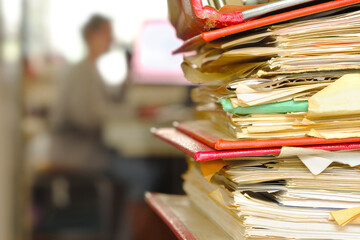 Stack of ring binders, file folders with workplace in the back. Beat the clock, deadlines, urgency, stress concept.Unrecognizable Person,free copy space.
