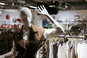 Fashion mannequin with disco ball in clothing store window.