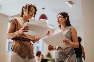 Two colleagues discuss and analyze printed documents in a contemporary workplace, exemplifying teamwork, professionalism, and collaboration during a business planning or decision-making session.