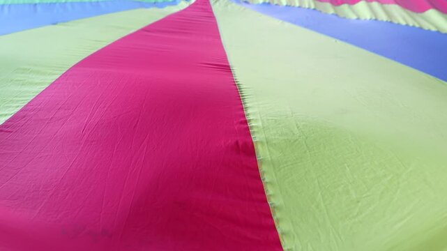 Colorful parachute fabric stretched and lifted, often used in children&rsquo;s games or activities, forming vibrant waves and patterns as it moves in the air.