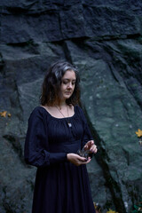 a woman in a black long dress near black rocks on Halloween holding a purple black crystal, performing a witch ritual, modern witch