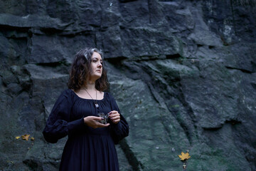 a woman in a black long dress near black rocks on Halloween holding a purple black crystal, performing a witch ritual, modern witch