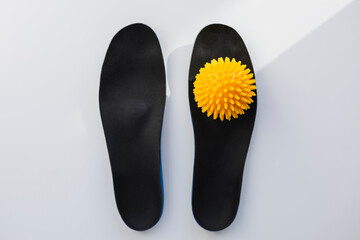 Top-down view of orthopedic shoe insoles and a foot massage ball on clean white.