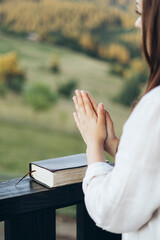 Woman praying with Bible on balcony overlooking peaceful mountain landscape.