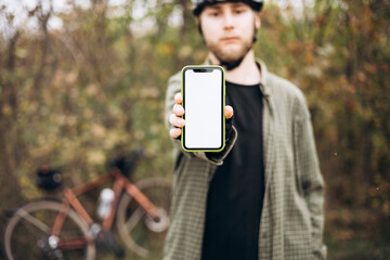 Cyclist in helmet holding smartphone with blank white screen and showing it.