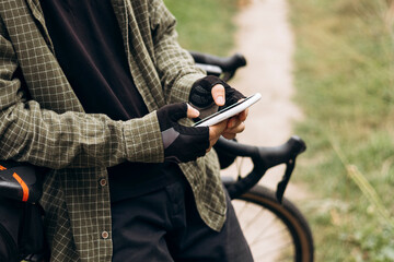 Man cyclist standing in a field using smartphone. Concept of outdoor technology.