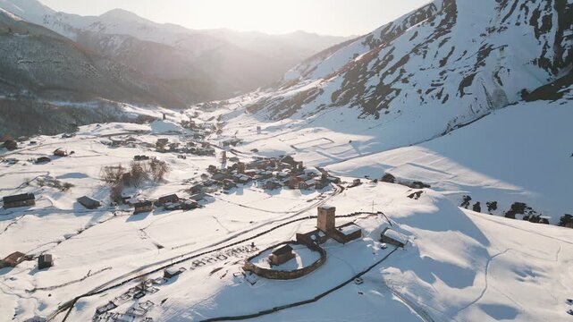 Aerial view Ancient Lamaria Monastery in snowy highland valley with Ushguli settlement village houses in cold winter land surrounded by Caucasus mountains. UNESCO - listed Upper Svaneti region