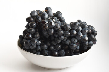 Bowl of fresh black grapes on white. High-resolution image of black grapes in a bowl on a white background, ideal for food and diet content.