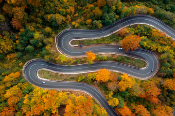 Aerial view of curving road through colorful autumn forest

