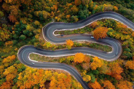 Aerial view of curving road through colorful autumn forest
