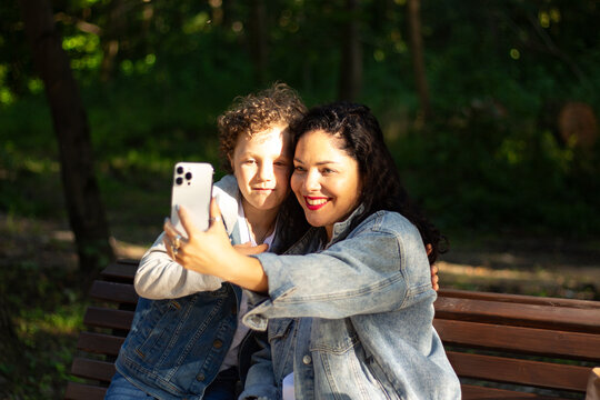 Mother making selfie together with her son. Taking selfie on smartphone. Smiling happy young family make photos outside in park to memorize moment. - Powered by Adobe