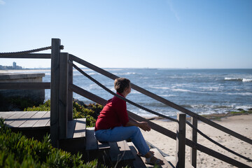 Middle-aged woman sitting on a wall looking at the ocean in Portugal, enjoying a sunny summer day