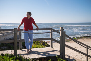 Middle-aged woman sitting on a wall looking at the ocean in Portugal, enjoying a sunny summer day
