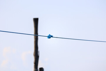 Simple blue nylon rope with knot tied on a wooden pole against a bright sky symbolizing connection or boundary