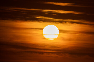 View of the glowing orb of the sun, a celestial pearl amidst a swirling canvas of fiery orange and smoky umber clouds, BerniÃ¨res-sur-Mer, Normandy, France.