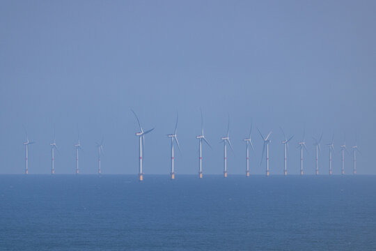 View of numerous wind turbines standing tall in the tranquil blue waters under a hazy sky, a testament to renewable energy, Berni&Atilde;&uml;res-sur-Mer, Normandy, France.