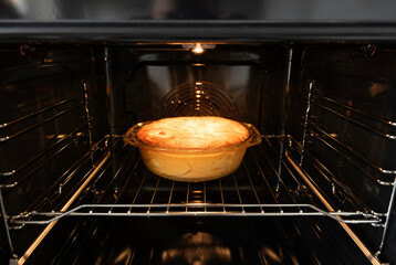 Fresh homemade pie baking in oven with golden crust. Hot dessert in glass dish inside modern kitchen appliance. Concept of cooking, baking, homemade food and delicious pastry preparation.