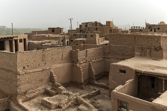 View of sun-baked mud structures and crumbling walls create a textured tapestry under a hazy sky in Gaotai Mud Homes, Xinjiang, China.