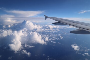 Obraz premium Soaring above fluffy clouds over vast blue ocean, airplane wing guides journey towards horizon, inspiring travel and adventure dreams