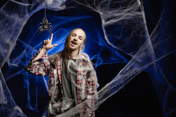 Creepy scary zombie man with ugly makeup holding finger in great idea or eureka sign standing on spooky spider web background. Halloween concept. Horror film.
