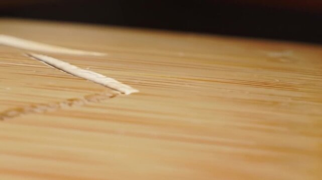 Close-up of light brown, parallel wood grain, likely from a cylindrical object, with a blurred dark background