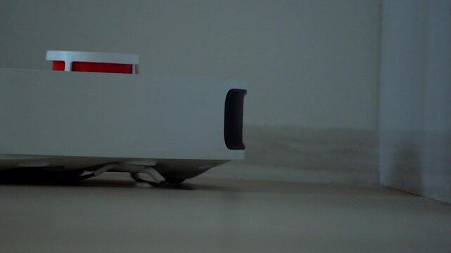 White robot vacuum cleaner cleaning the floor in a modern apartment. Smart home technology for automatic cleaning and housekeeping. Close-up of an autonomous robotic hoover.