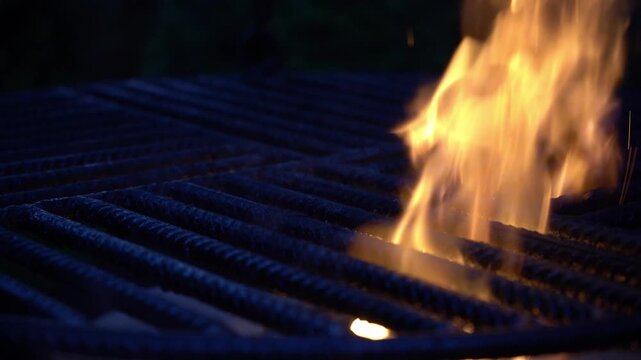 Flames rising through metal grill grates in a dark scene, capturing intense heat, fire motion, and dramatic barbecue atmosphere with strong contrast and texture.