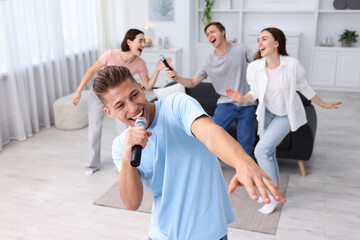 Obraz premium Young man singing karaoke with friends at home, selective focus