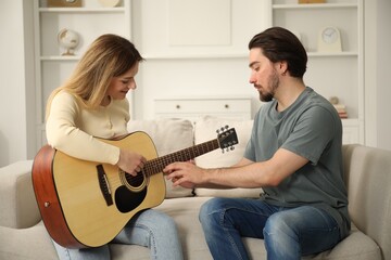 Tutor teaching woman to play guitar on sofa at home