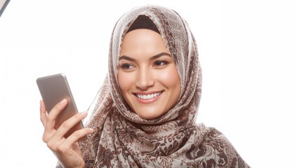 Smiling Muslim woman wearing a patterned headscarf holding a smartphone while looking at the device against a bright white background