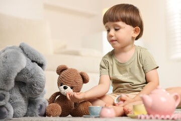 Cute little boy playing tea party with his toys indoors