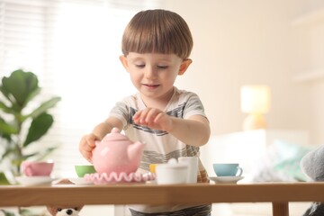 Cute little boy playing with toy tea set at table indoors