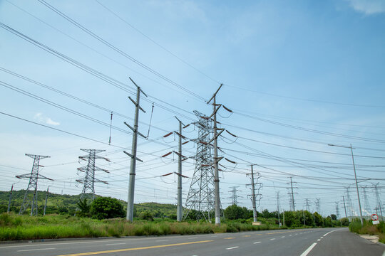 High-voltage transmission towers along a rural road under blue sky