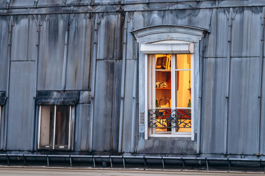 Illuminated window of a Parisian mansard apartment, with warm light shining from inside against the classic zinc rooftops of the city