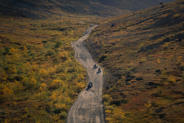 ATV riders traveling along a winding dirt road in the autumn tundra, with mountains in the background. Travel in Lapland