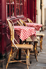 Small outdoor terrace of a Parisian café in the 6th arrondissement with red-checkered tablecloths and classic rattan chairs by a painted wooden facade