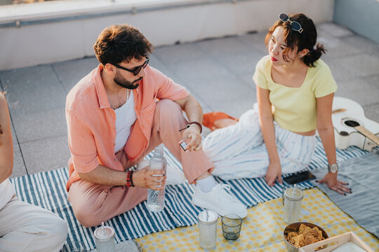 Group of young friends enjoying a casual rooftop picnic, chatting and relaxing outdoors in the warm sunlight. Perfect spot to unwind and share moments with a small group of close companions.