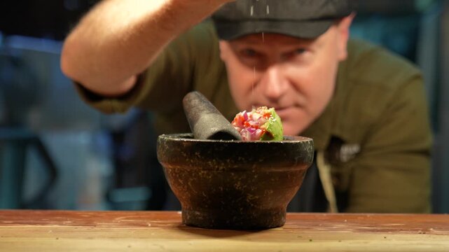 Chef seasoning guacamole in a traditional stone mortar