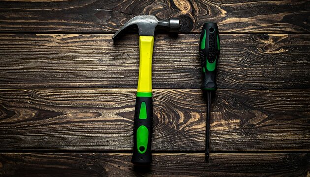 A hammer and screwdriver rest side-by-side on a dark wooden surface with a natural grain pattern