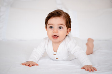 a baby on a white bed at home, a place for text, a cute smiling little child getting ready for bed, a portrait of a little boy child