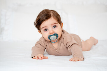 A baby sucks a pacifier on a white bed at home, a place for text