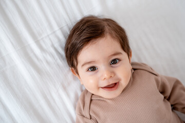 a baby, a close-up portrait of a smiling or laughing baby boy on a white bed, a place for text