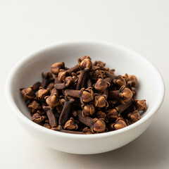 A white bowl of whole dried cloves, isolated on a white background.