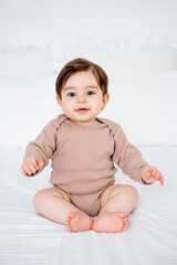Smiling baby boy on the bed at home, cute little baby sitting on the white bed